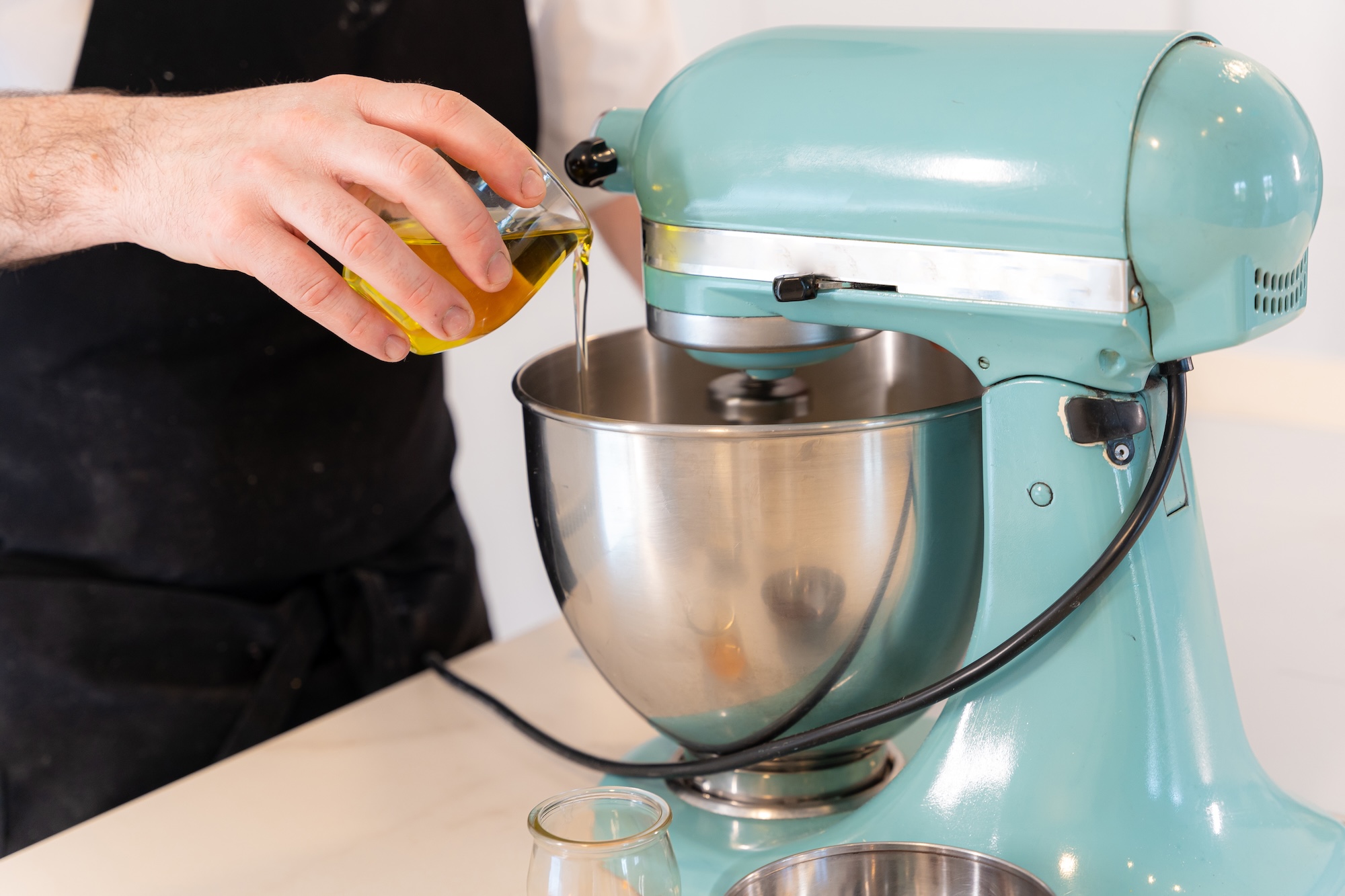A man baking a red velvet cake at home, preparing the cake by adding oil in a teal stand mixer with a stainless steel bowl.